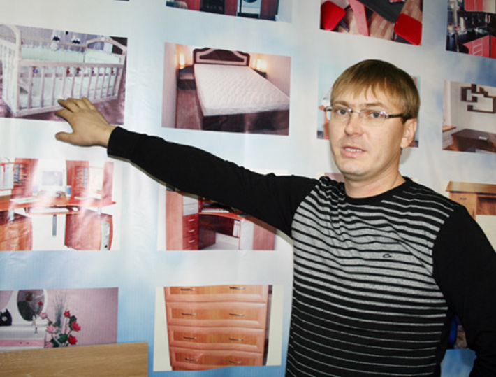 Сергей Седлецкий демонстрирует ассортимент своих товаров, запечатленный на специальном стенде.