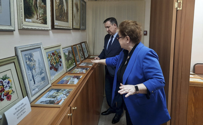 Председатель совета ветеранов Колыванского района Александра Афанасьева знакомит главу района Евгения Артюхова с выставкой в галерее центра ветеранов. Фото: vk.com